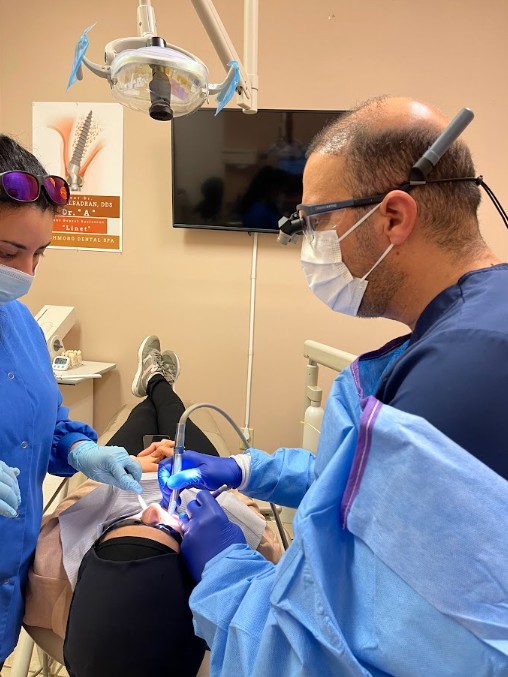 Dr. Firas Albadran and dental assistant performing treatment together in the operatory at Richmond Dental Spa — team-based dental care with magnification loupes