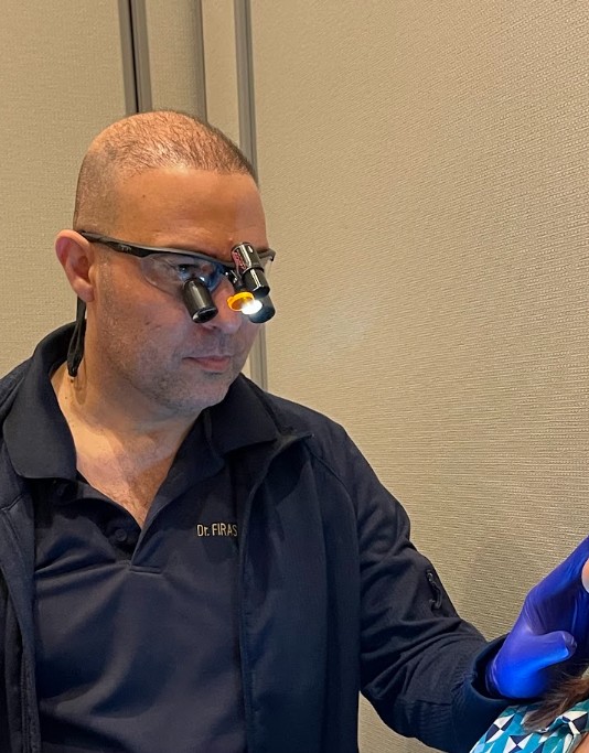 Dr. Firas Albadran performing myofascial pain assessment and masseter muscle palpation on a patient at Richmond Dental Spa wearing illuminated magnification loupes