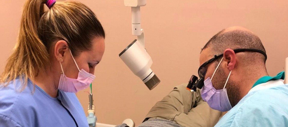 Dr. Firas Albadran and dental assistant working together in the operatory at Richmond Dental Spa — wide angle view showing Zumax surgical microscope